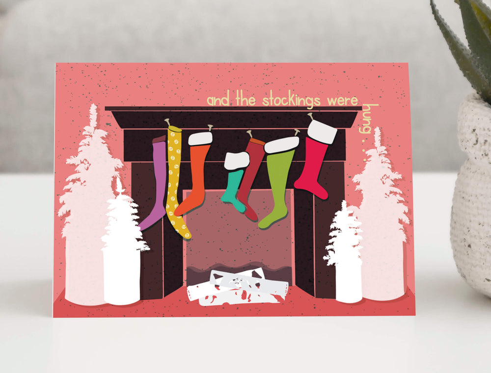 Festive holiday greeting card featuring a cozy Christmas fireplace with five colorful stockings hanging from the dark brown mantel. 