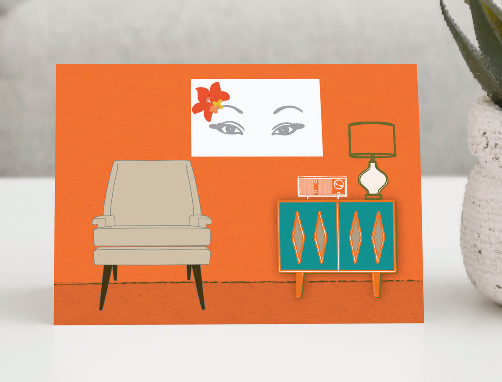 Mid-century modern greeting card featuring a vintage-inspired living room scene with a retro chair, teal cabinet, lamp, and wall art on an orange background. 